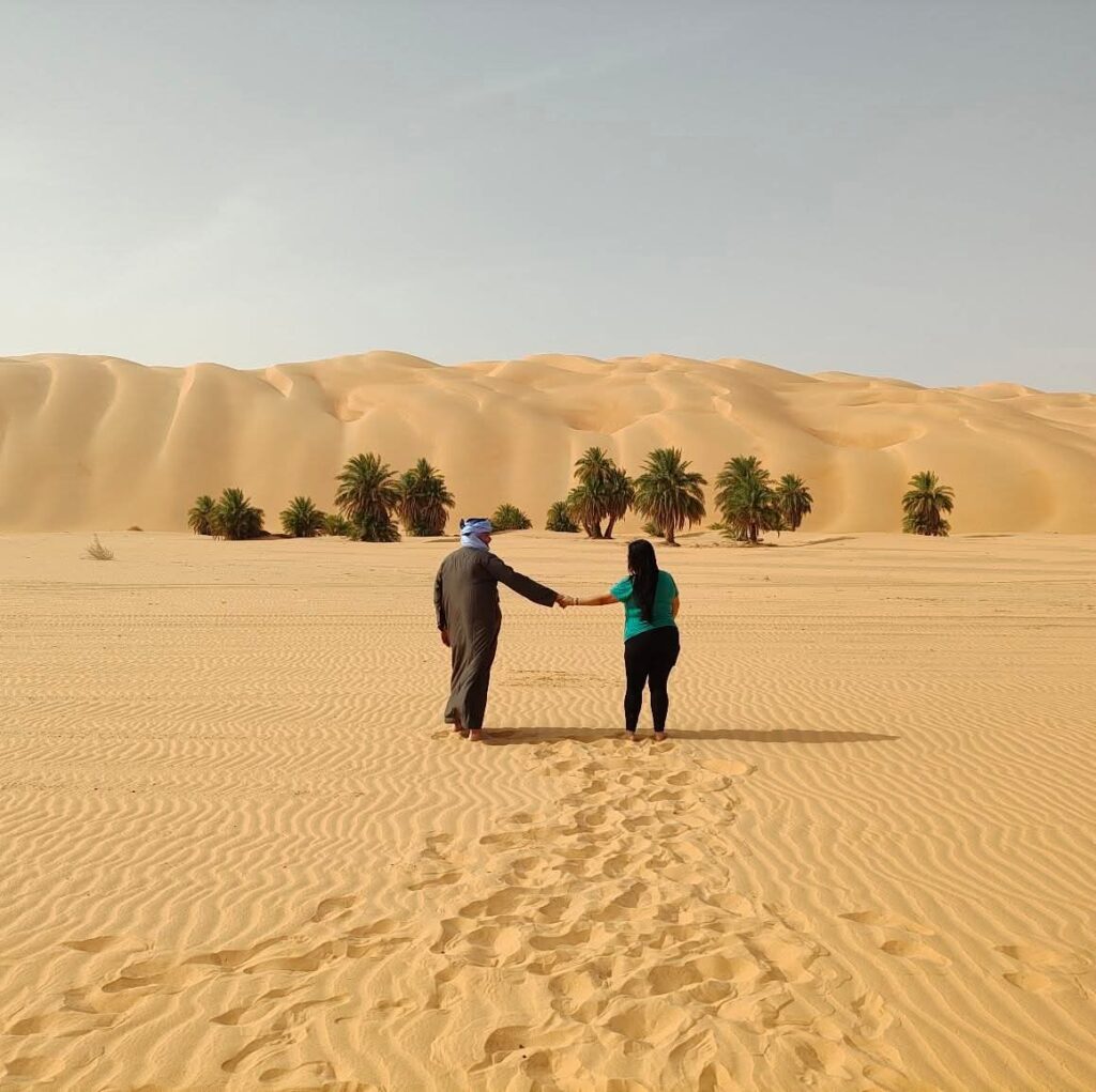 A couple holds hands in front of the Big Dunes of Azoueiga