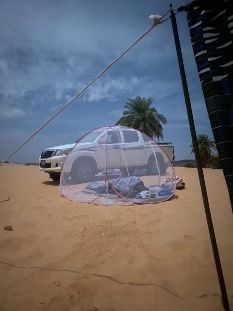 A traveler sits in a bug net on the desert floor of the Big Dunes of Azoueiga