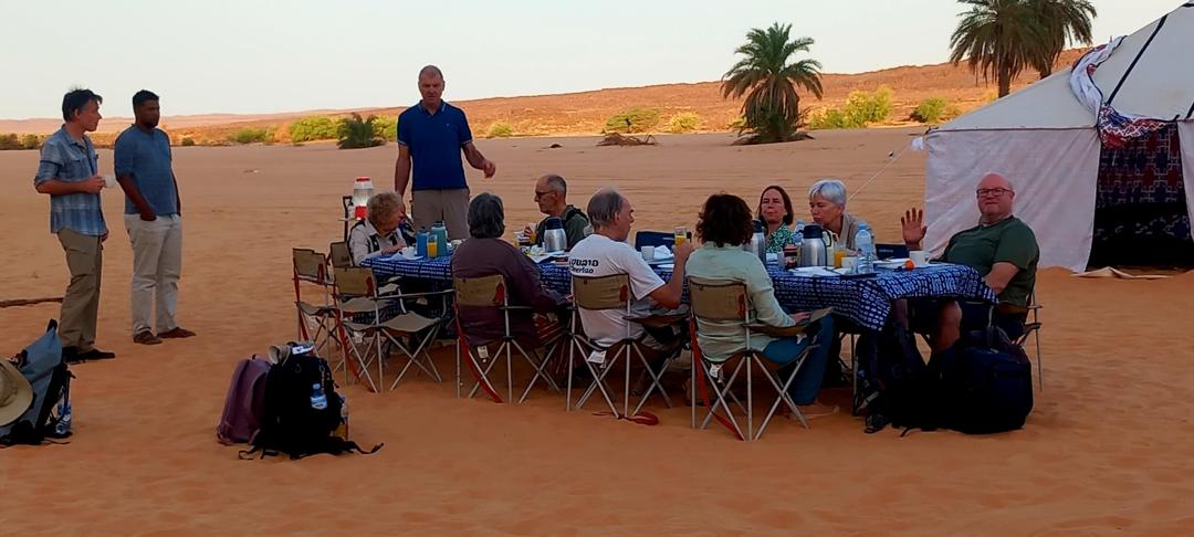 A tour group sits around a table eating dinner and socializing