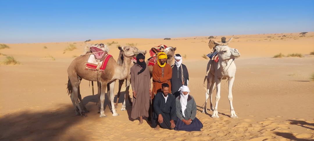 A small group poses with camels in front of the open desert