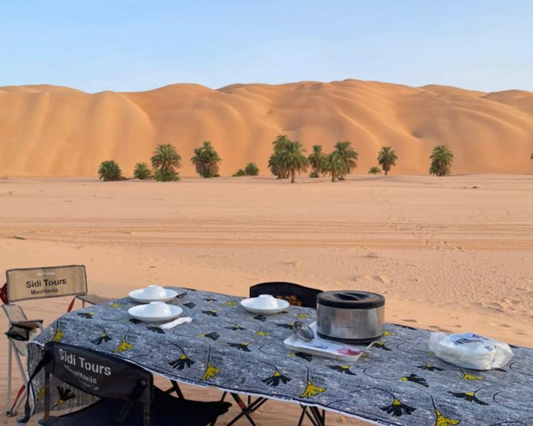 A dinner table is set in the foreground of the Big Dunes of Azoueiga